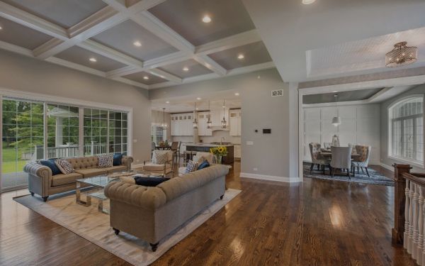 A cozy living room with a tufted sofa, glass coffee table, and large windows, leading to a dining area. hardwood floor refinishing and sanding professionals